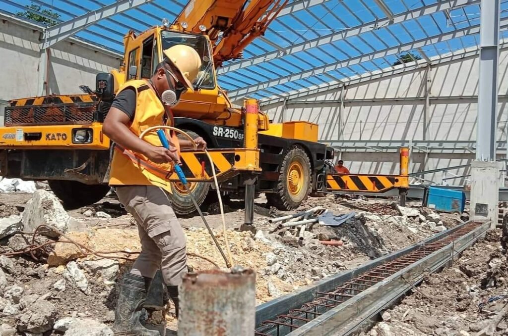 Worker conducting soil poisoning treatment at construction site using termite barrier methods to prevent future infestation.